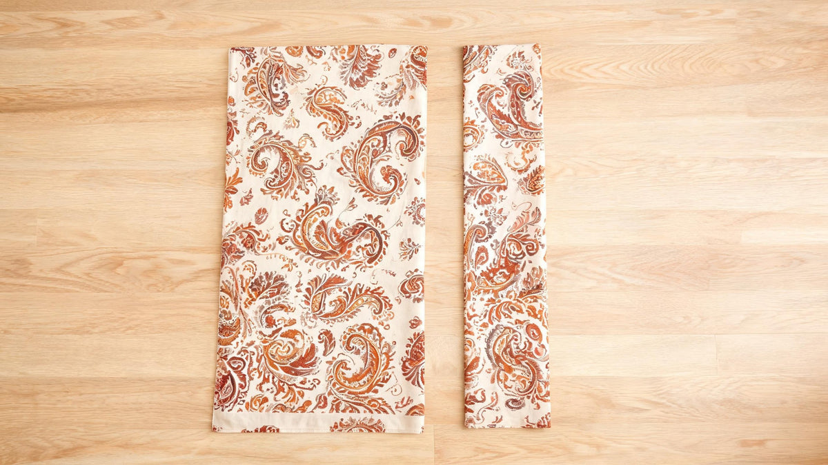 A wide paisley shawl and a narrow paisley stole laid flat side by side on a pale oak table