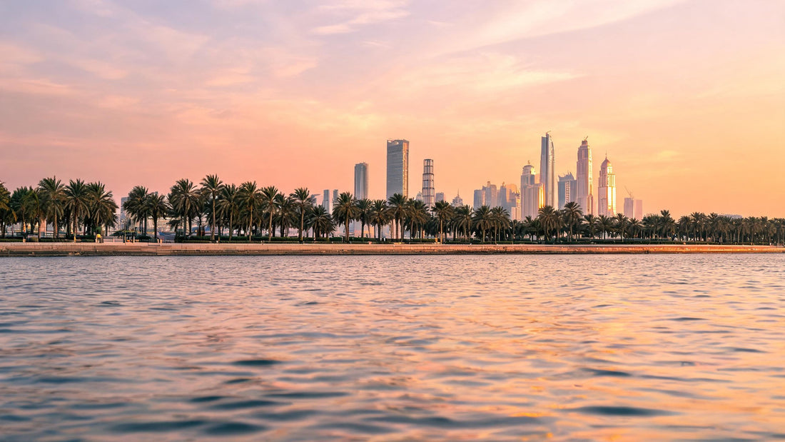 Abu Dhabi skyline across the water at sunset, with palm trees along the Corniche