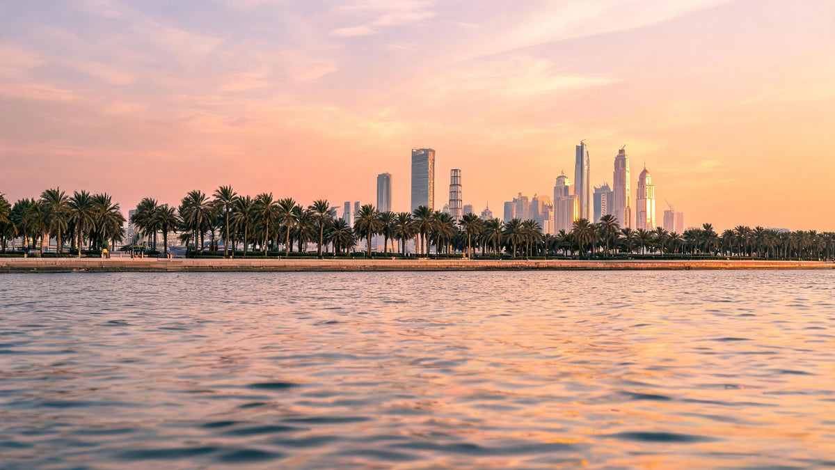 Abu Dhabi skyline across the water at sunset, with palm trees along the Corniche