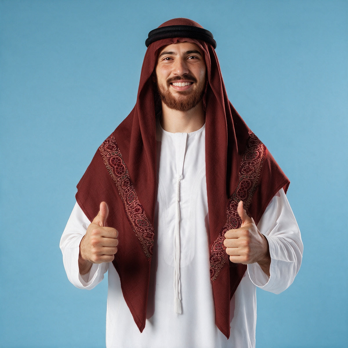 Man wearing the Barquq Kashmiri pashmina ghutra in burgundy with a black agal and white thobe, copper rose sozni border on each front end