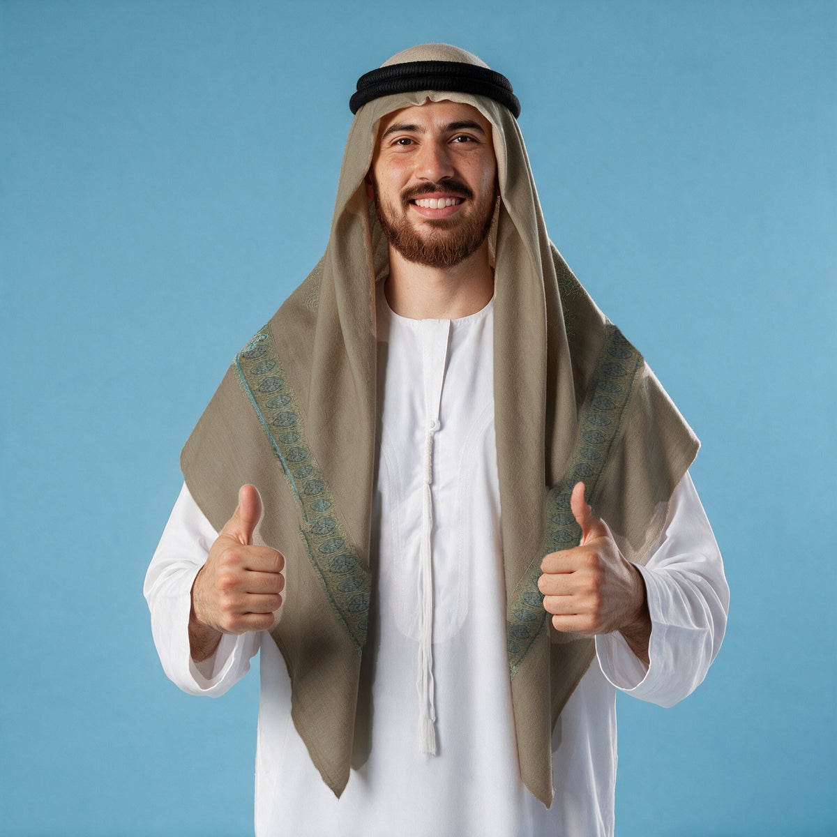 Man wearing the Zabarjad Kashmiri pashmina ghutra in taupe with a black agal and white thobe, aqua turquoise sozni border on each front end