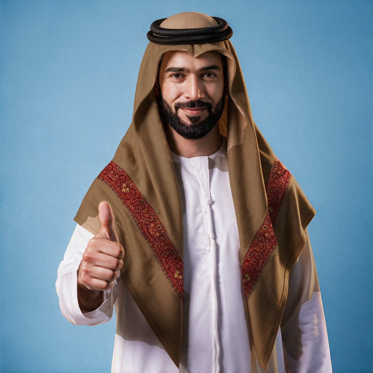 Man wearing the Qahwa Kashmiri pashmina ghutra in coffee brown with a black agal and white thobe, bright red and gold sozni border on each front end
