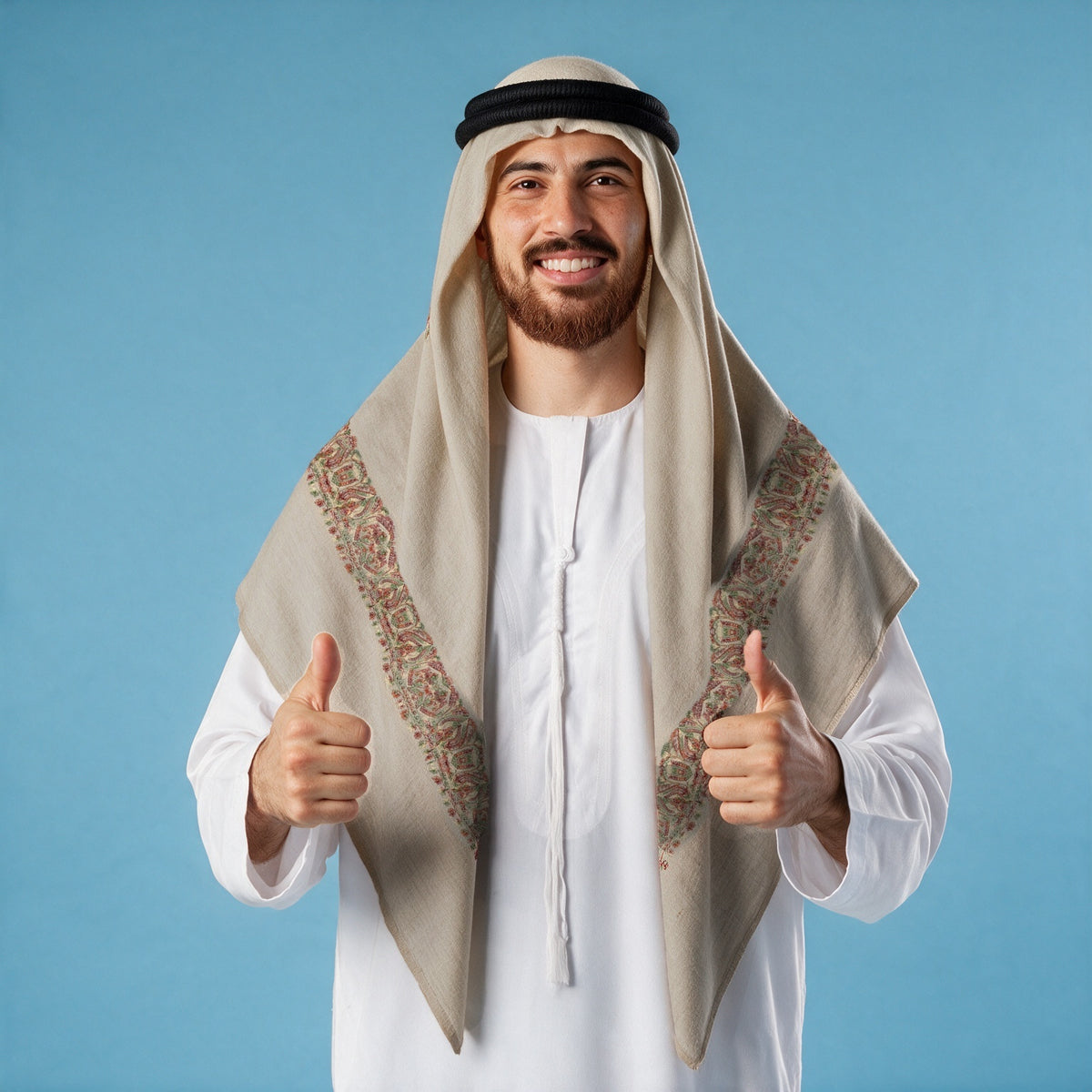 Man wearing the Shaqaiq Qalam Kaari Super Turma Kashmiri semi pashmina in light greige with a black agal and white thobe, rust red, olive green and cream multicolour pen-work border on each front end