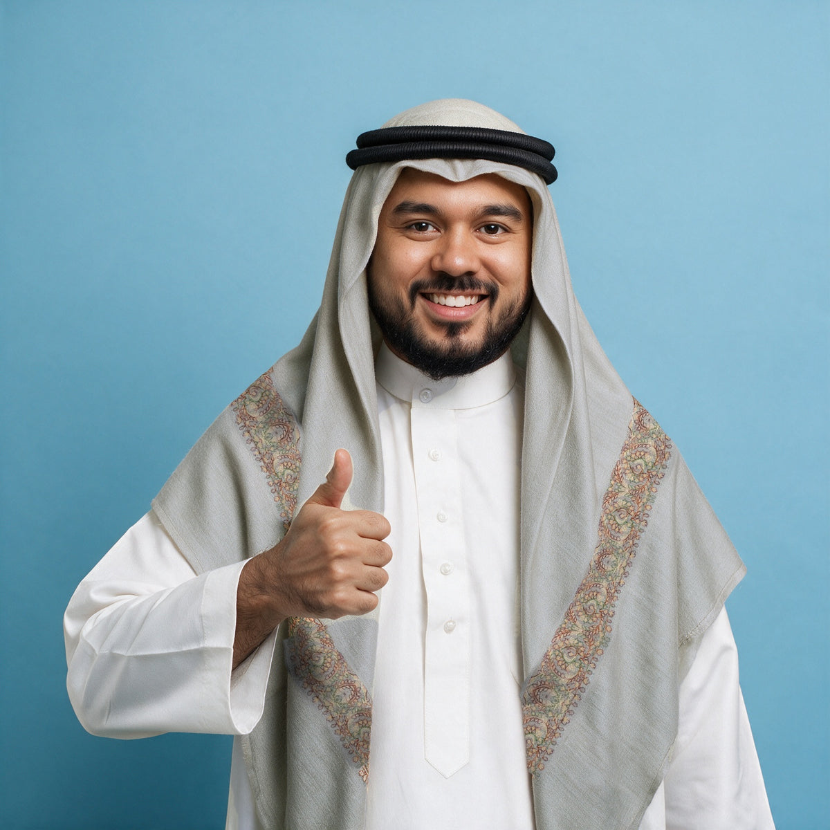 Man wearing the Narjis Qalam Kaari Super Turma Kashmiri semi pashmina in pale sage grey with a black agal and white thobe, pastel peach, rust, olive and pale gold multicolour pen-work border on each front end