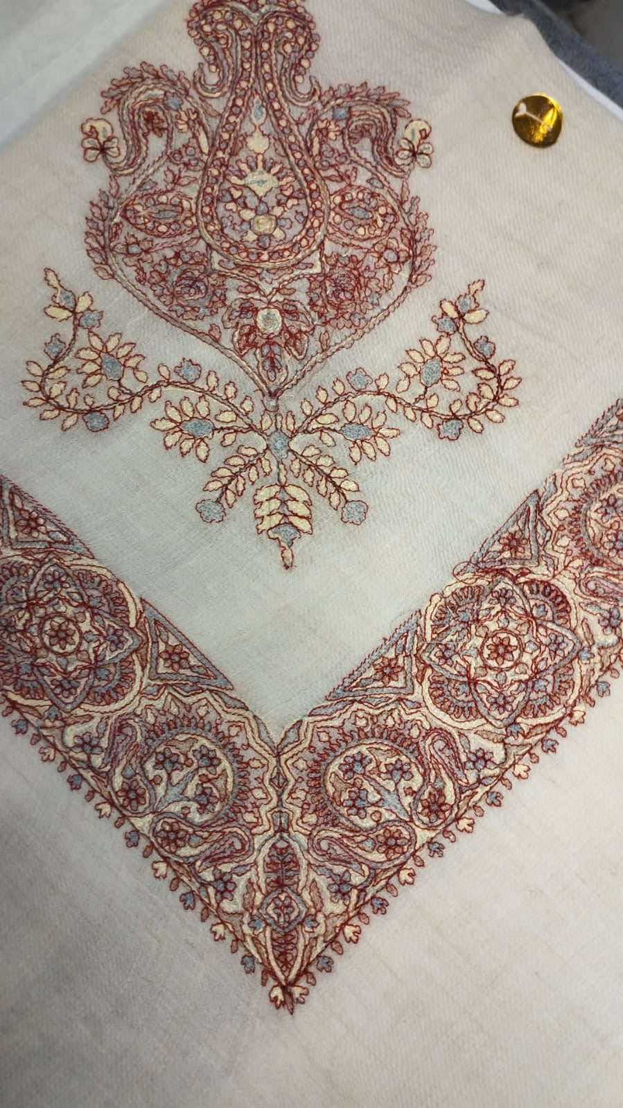 Qasida Qalam Kaari Pashmina folded to a point at the corner, showing the madder red, cream and slate blue paisley motif and rosette border