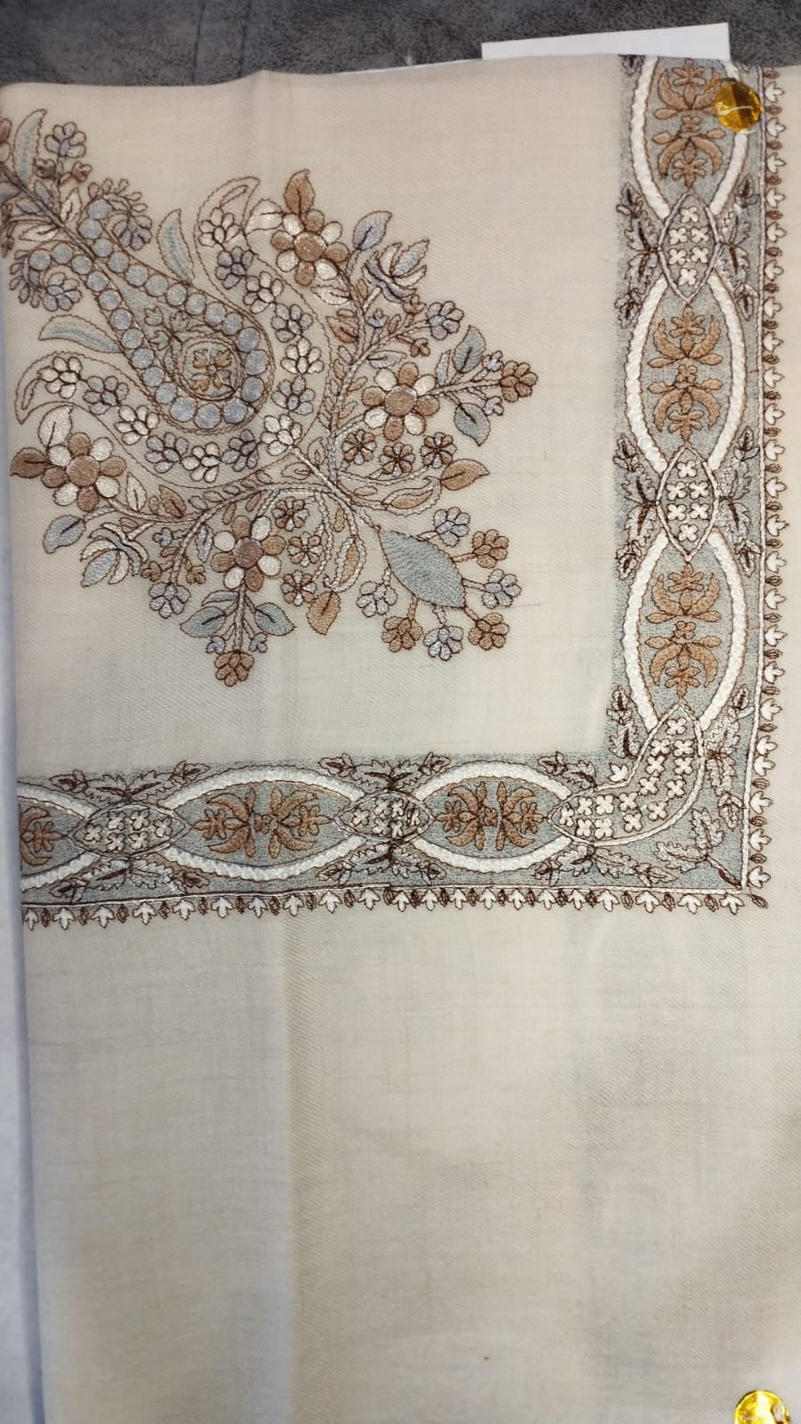 Qirtas Qalam Kaari Pashmina laid flat, taupe, pale blue-grey and ivory floral bouquet corner motif and interlaced ribbon border on a natural oatmeal ground