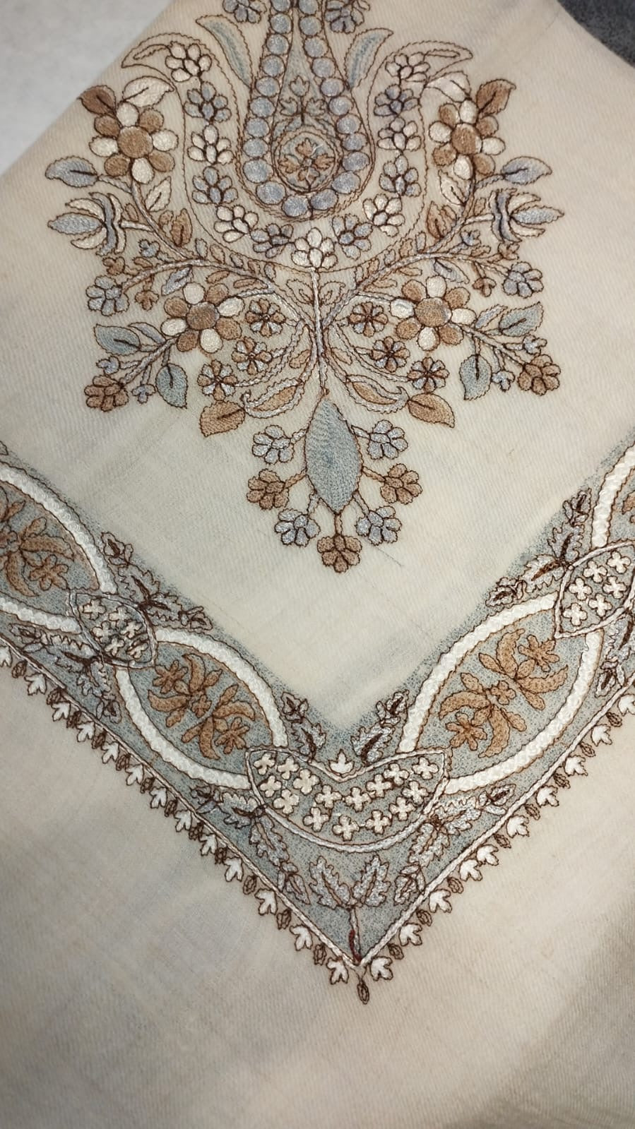 Qirtas Qalam Kaari Pashmina folded to a point at the corner, showing the taupe, pale blue-grey and ivory floral bouquet motif and interlaced ribbon border
