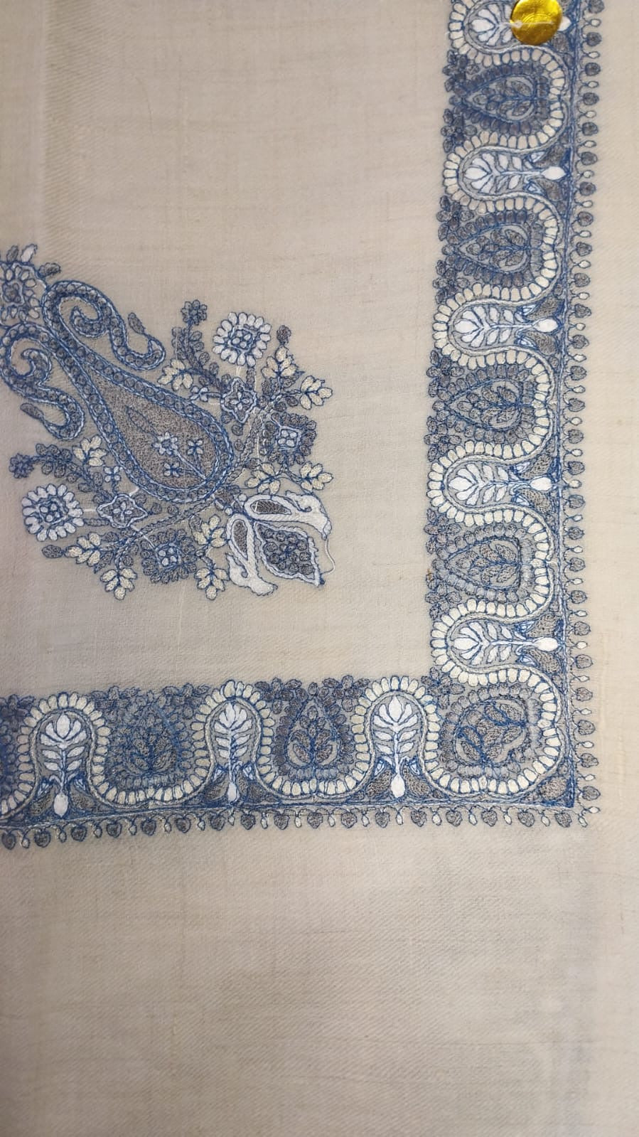 Mihbara Qalam Kaari Pashmina laid flat, faded indigo and ivory paisley corner motif and winding paisley border on a natural oatmeal ground