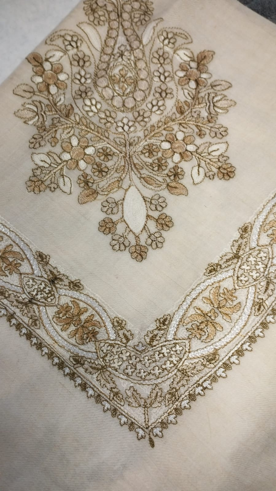 Wadi Qalam Kaari Pashmina folded to a point at the corner, showing the camel, fawn and ivory floral bouquet motif and interlaced ribbon border