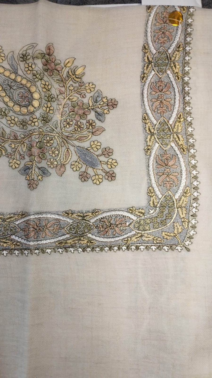 Zanbaq Qalam Kaari Pashmina laid flat, butter yellow, dusty rose and grey-blue floral bouquet corner motif and interlaced ribbon border on a natural oatmeal ground