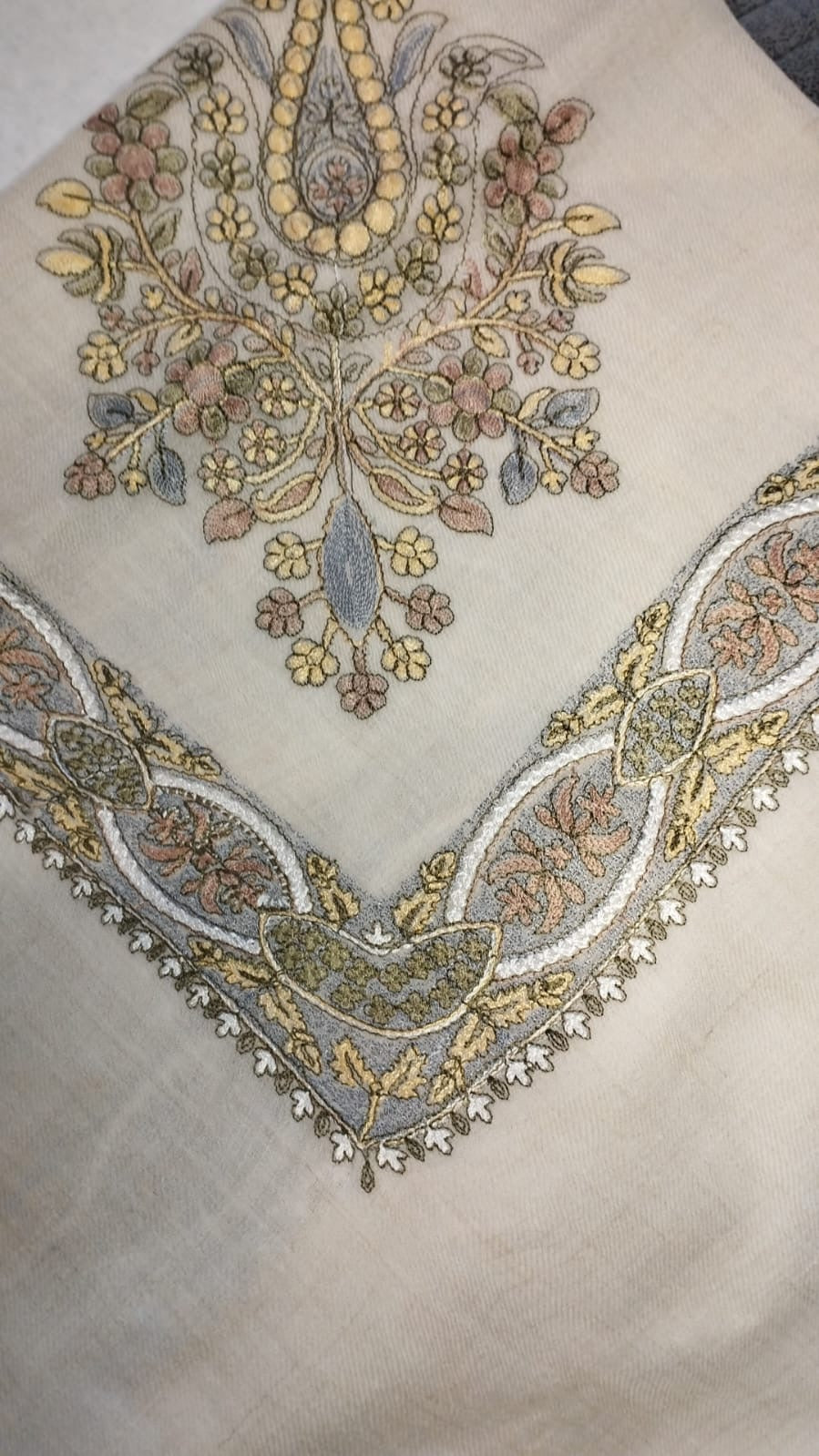 Zanbaq Qalam Kaari Pashmina folded to a point at the corner, showing the butter yellow, dusty rose and grey-blue floral bouquet motif and interlaced ribbon border