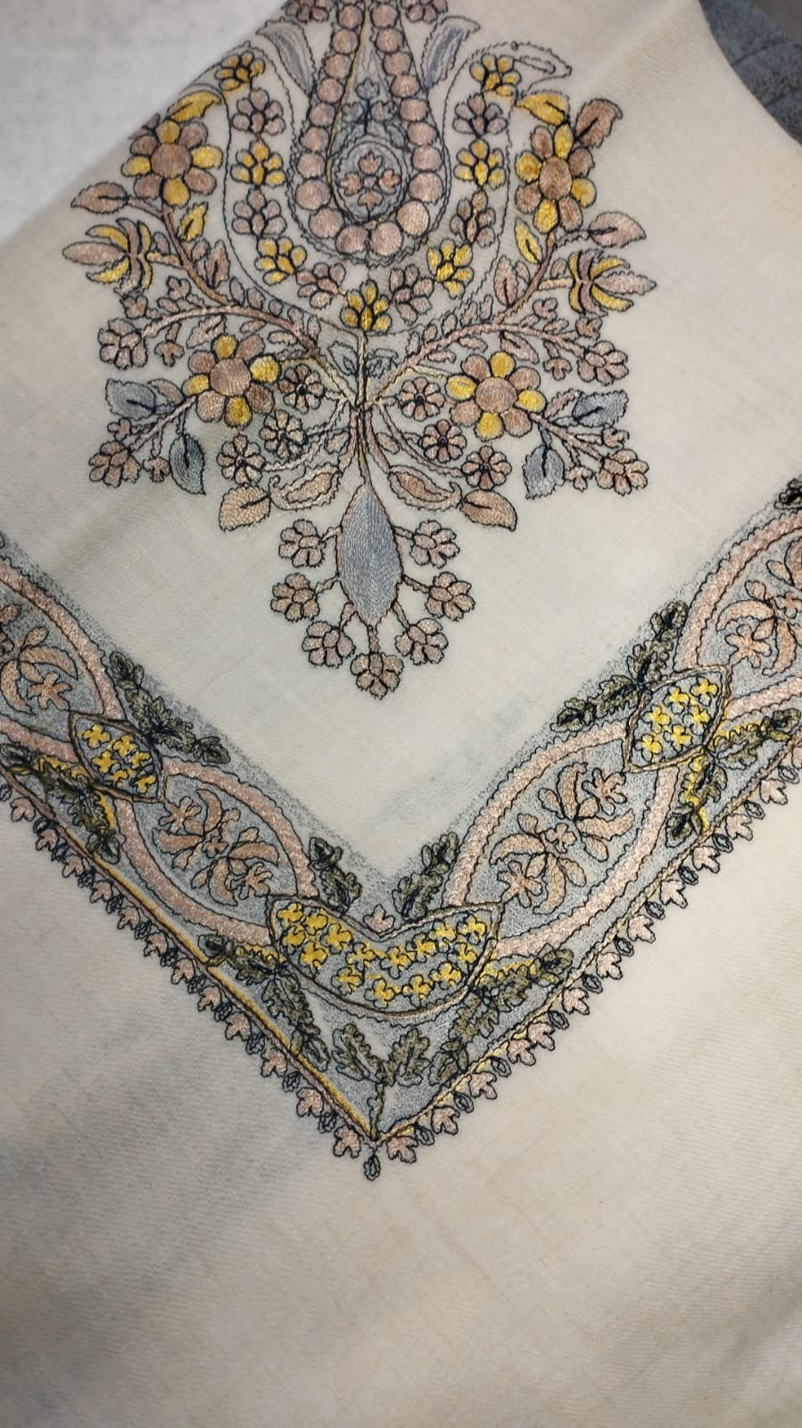 Hikaya Qalam Kaari Pashmina folded to a point at the corner, showing the blush pink, yellow and grey-blue floral bouquet motif and interlaced ribbon border