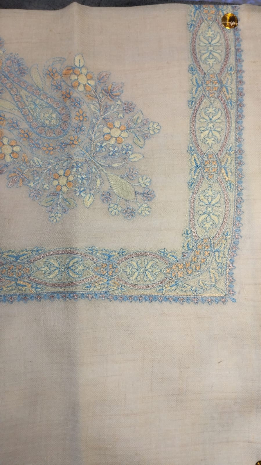 Sepehr Qalam Kaari Pashmina laid flat, pale sky blue, lilac and apricot floral bouquet corner motif and interlaced ribbon border on a natural oatmeal ground