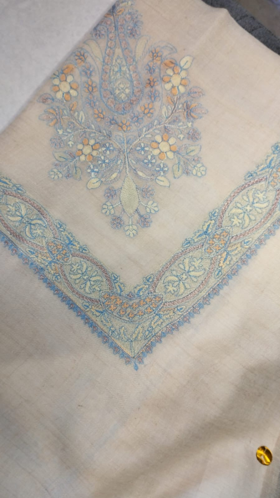Sepehr Qalam Kaari Pashmina folded to a point at the corner, showing the pale sky blue, lilac and apricot floral bouquet motif and interlaced ribbon border