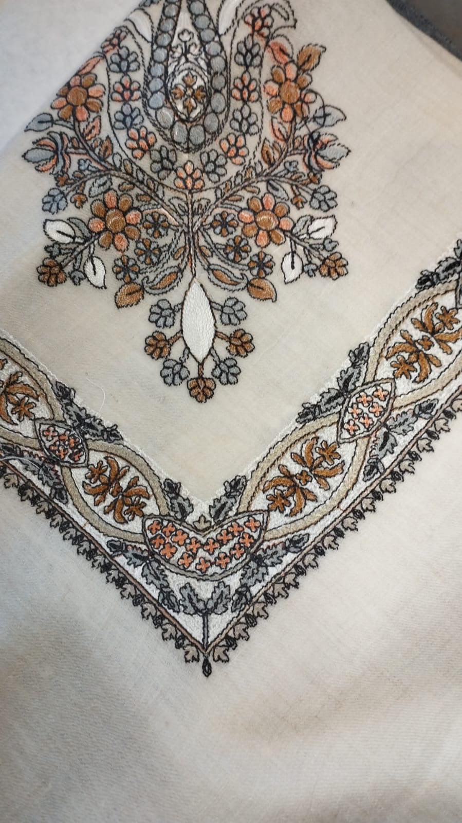 Mijmar Qalam Kaari Pashmina folded to a point at the corner, showing the burnt orange, slate and charcoal floral bouquet motif and interlaced ribbon border