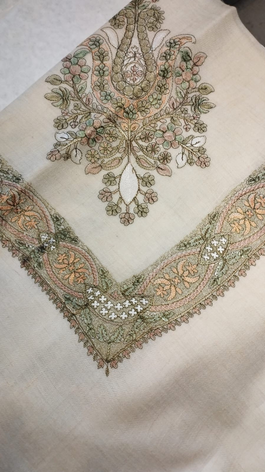 Safsaf Qalam Kaari Pashmina folded to a point at the corner, showing the sage green and peach floral bouquet motif and interlaced ribbon border