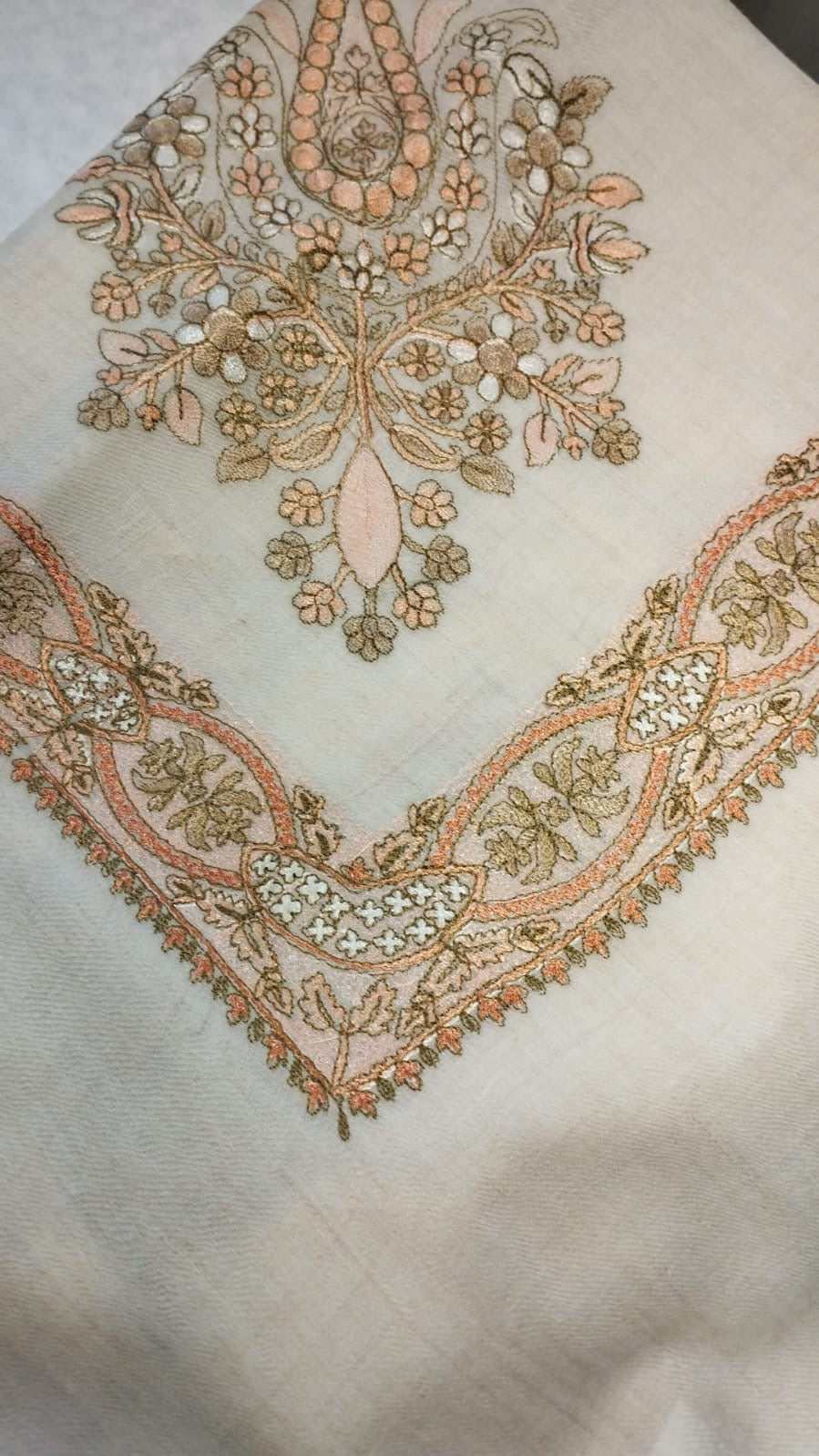 Rubai Qalam Kaari Pashmina folded to a point at the corner, showing the apricot and olive floral bouquet motif and interlaced ribbon border