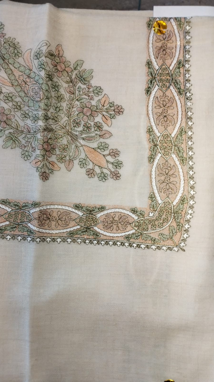 Nastaliq Qalam Kaari Pashmina laid flat, dusty pink, sage and ivory floral bouquet corner motif and interlaced ribbon border on a natural oatmeal ground