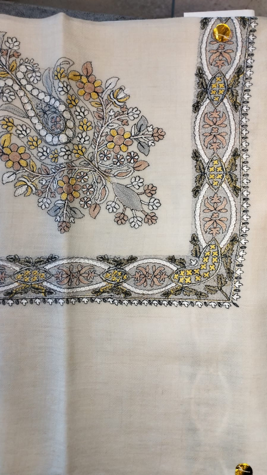 Simurgh Qalam Kaari Pashmina laid flat, saffron yellow, grey-blue and rose floral bouquet corner motif and interlaced ribbon border on a natural oatmeal ground