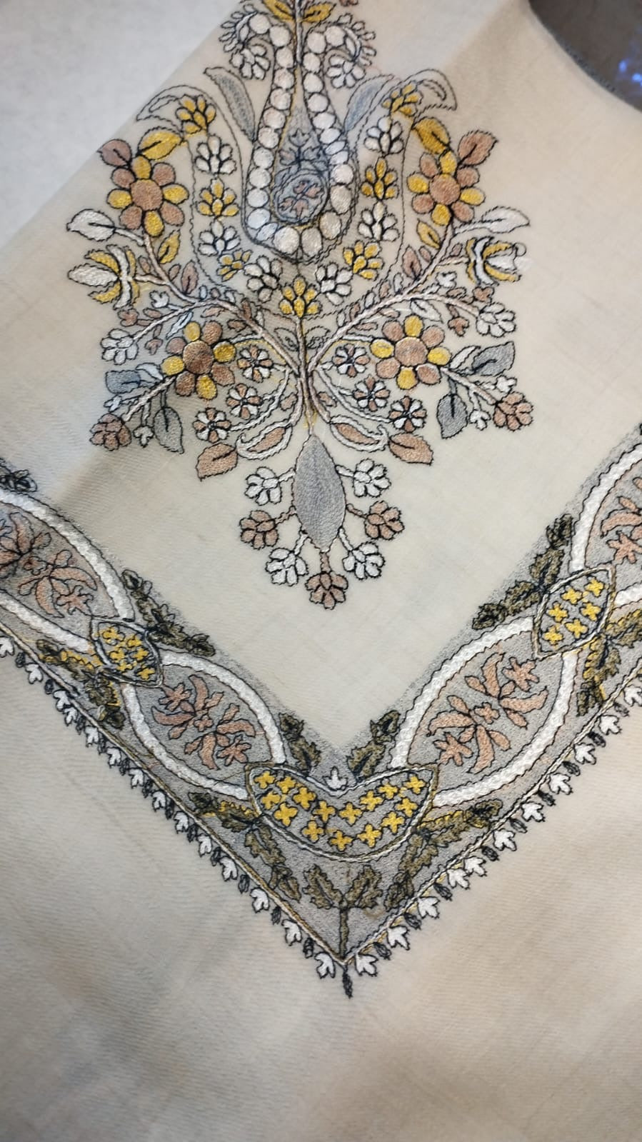 Simurgh Qalam Kaari Pashmina folded to a point at the corner, showing the saffron yellow, grey-blue and rose floral bouquet motif and interlaced ribbon border