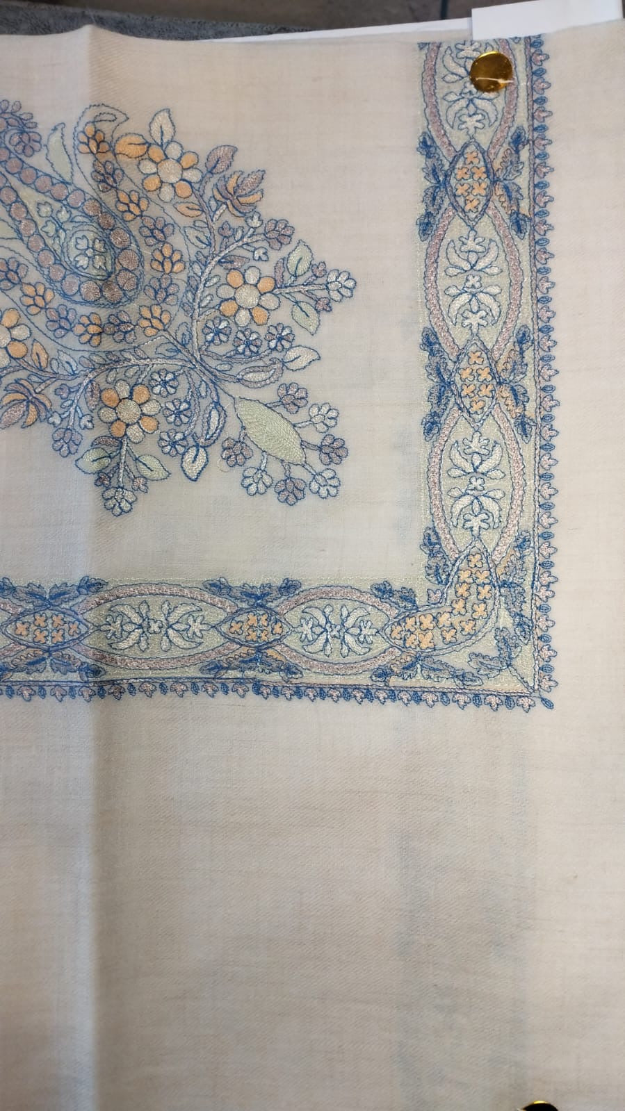 Marsa Qalam Kaari Pashmina laid flat, sky blue and apricot floral bouquet corner motif and interlaced ribbon border on a natural oatmeal ground
