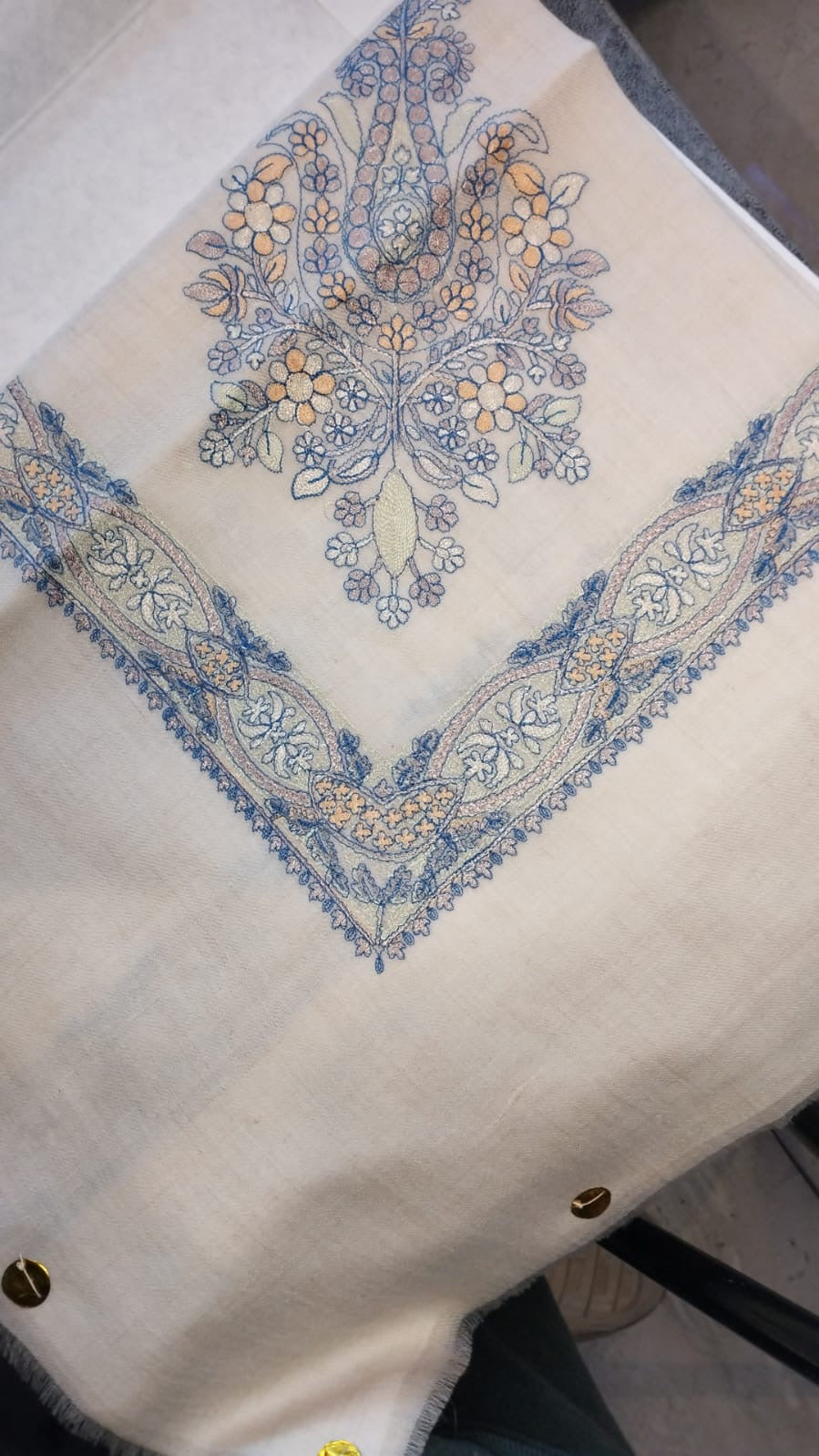 Marsa Qalam Kaari Pashmina folded to a point at the corner, showing the sky blue and apricot floral bouquet motif and interlaced ribbon border