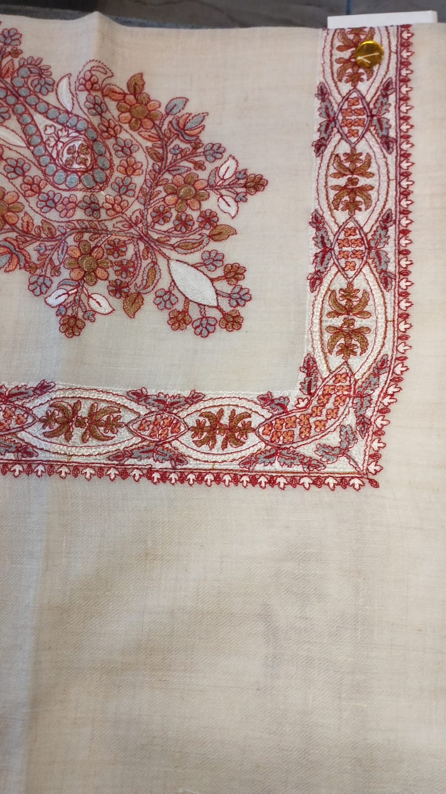 Diwani Qalam Kaari Pashmina laid flat, scarlet, rust and grey-blue floral bouquet corner motif and interlaced ribbon border on a natural oatmeal ground