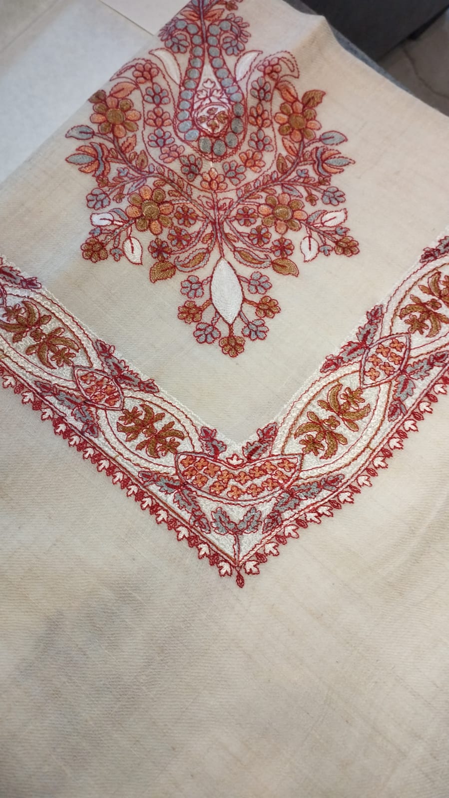 Diwani Qalam Kaari Pashmina folded to a point at the corner, showing the scarlet, rust and grey-blue floral bouquet motif and interlaced ribbon border