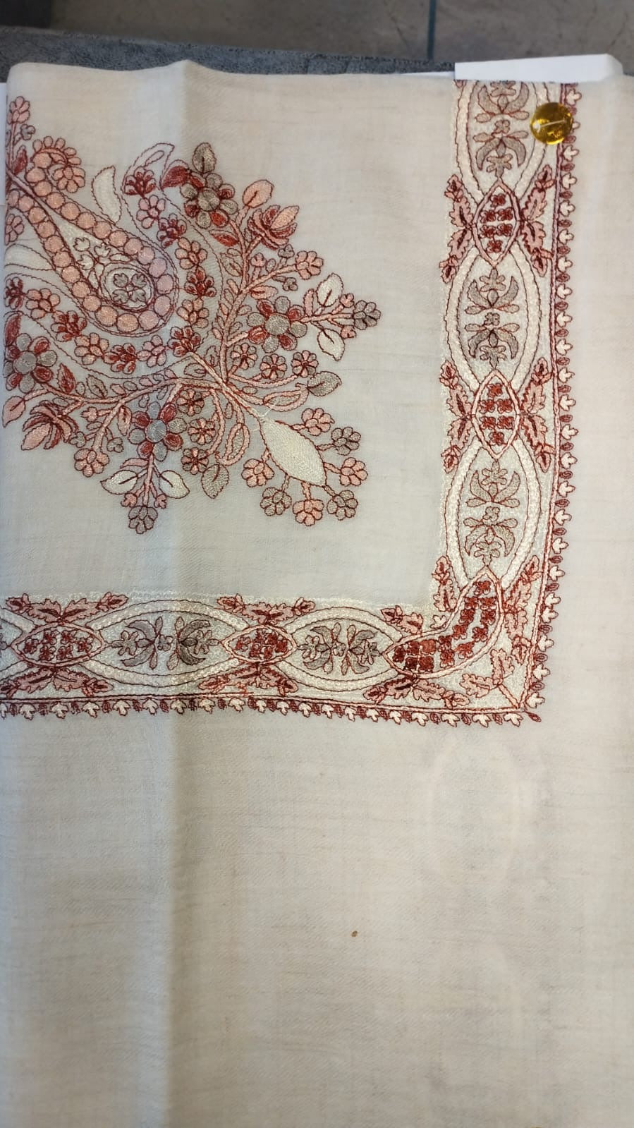 Hashiya Qalam Kaari Pashmina laid flat, brick red, rose and taupe floral bouquet corner motif and interlaced ribbon border on a natural oatmeal ground
