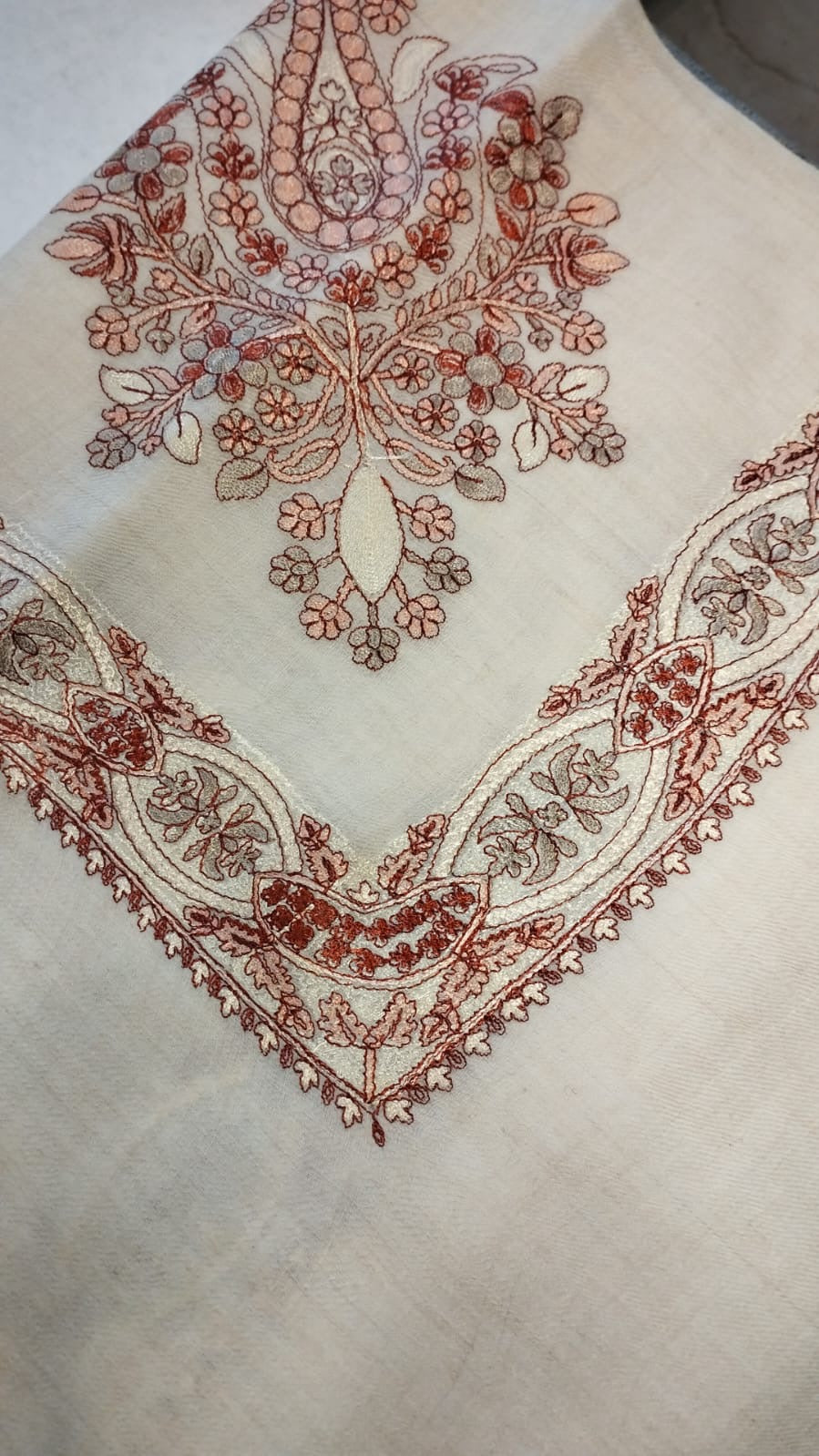 Hashiya Qalam Kaari Pashmina folded to a point at the corner, showing the brick red, rose and taupe floral bouquet motif and interlaced ribbon border